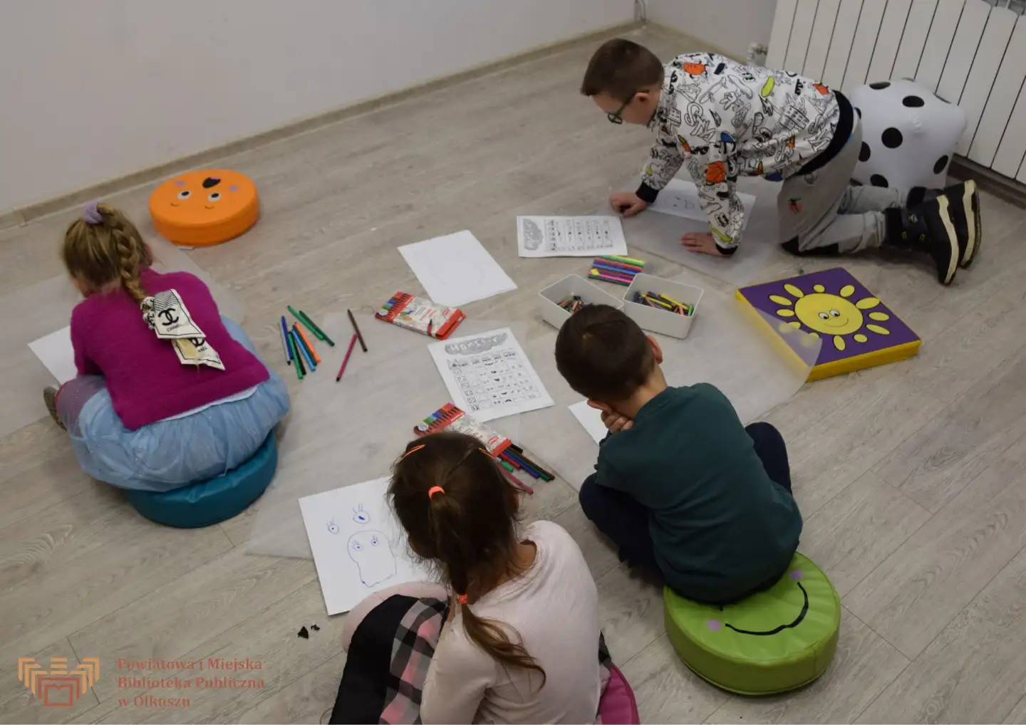 Zdjęcie zrobione w trakcie zajęć Zabawy z książką po angielsku. Czwórka dzieci siedzi na podłodze i rysuje potwory.