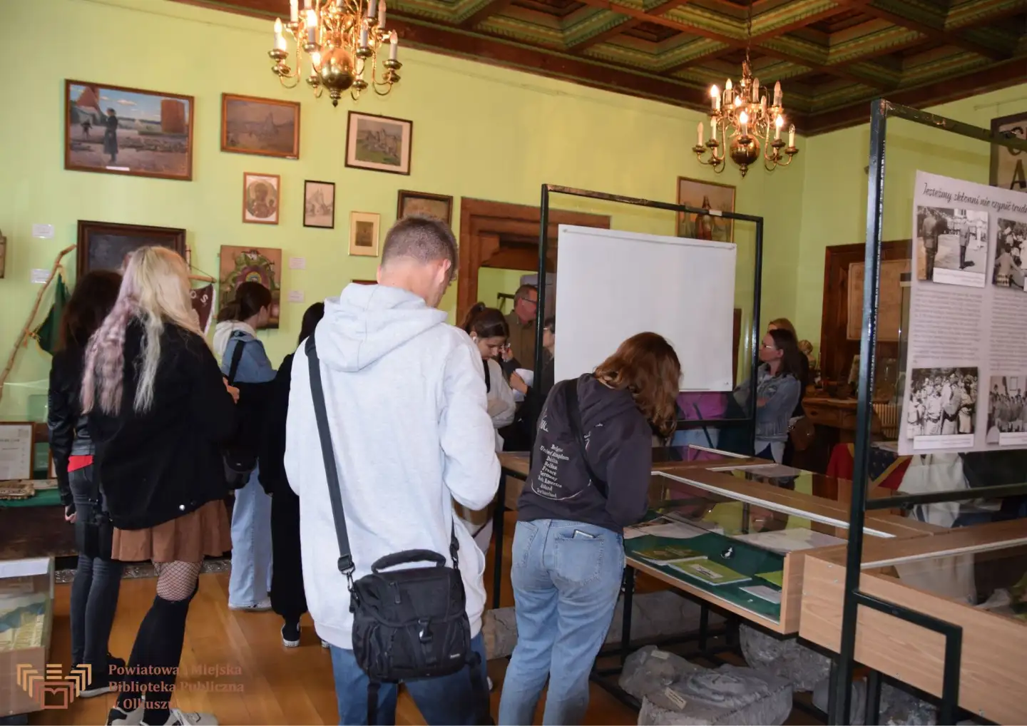 Zdjęcie przedstawia młodzież oglądającą eksponaty w muzeum.